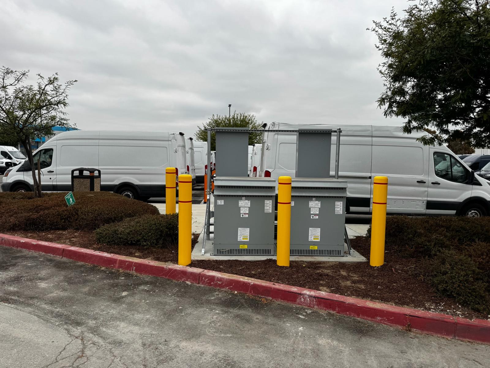 Fleet vans parked beside paired electrical enclosures protected by yellow bollards