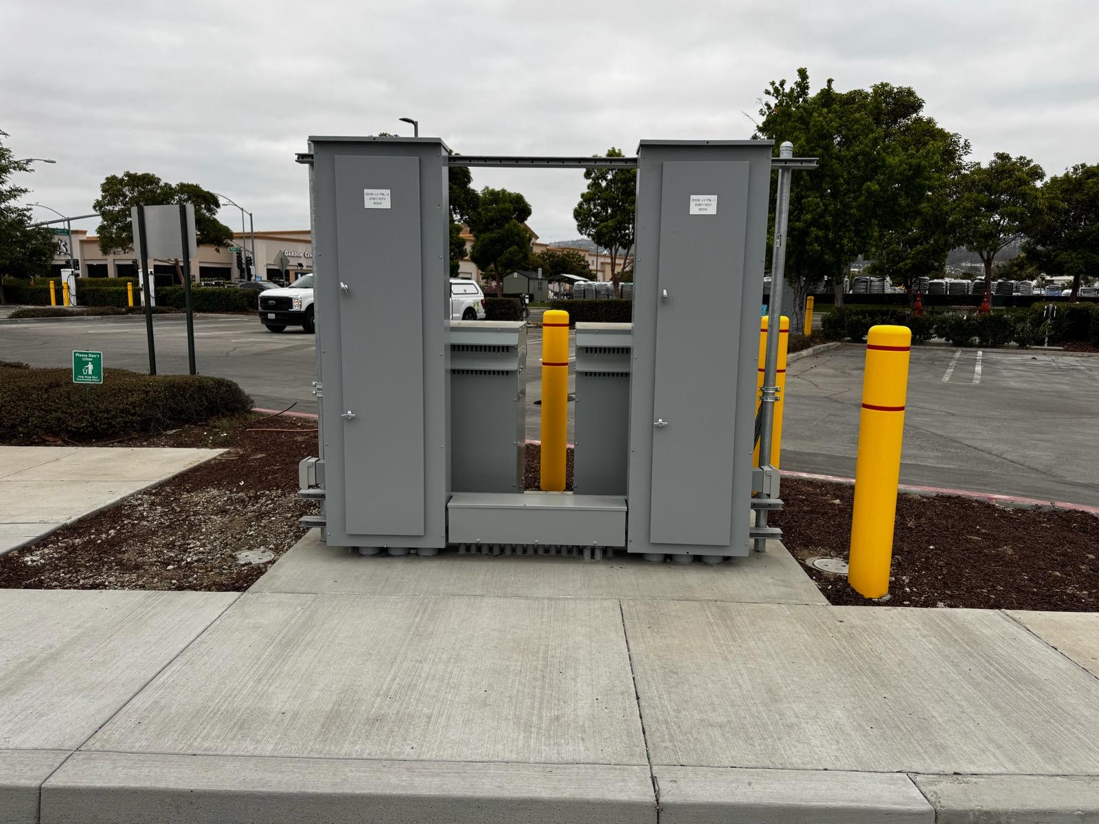 Paired low-voltage panel enclosures behind yellow bollards at a commercial site